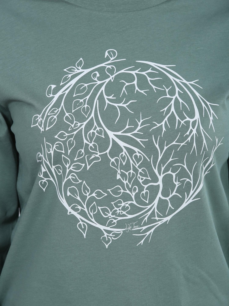 A close-up image of a person wearing a green t-shirt with a white circular design featuring a tree-like pattern.