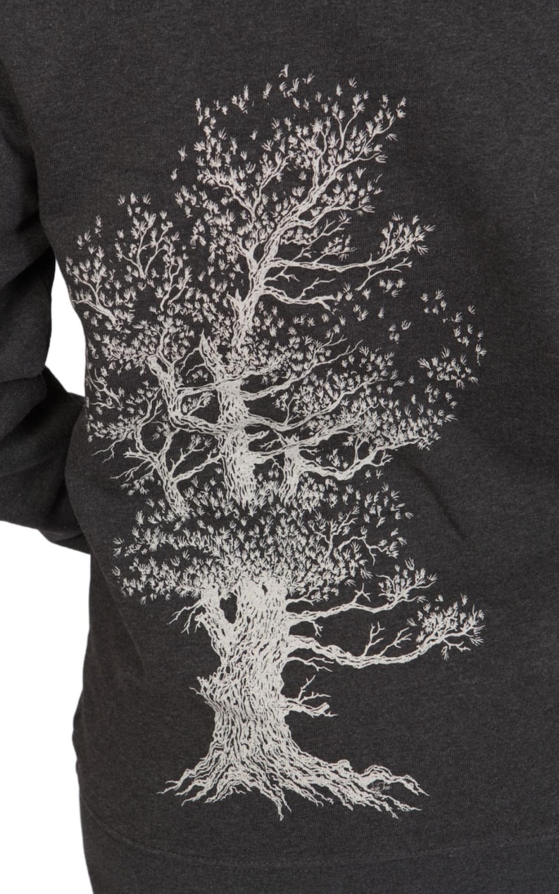a close-up view of a person wearing a grey sweatshirt with a white tree design on the back.