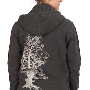 A woman wearing a gray hooded sweatshirt with a white tree design on the back.