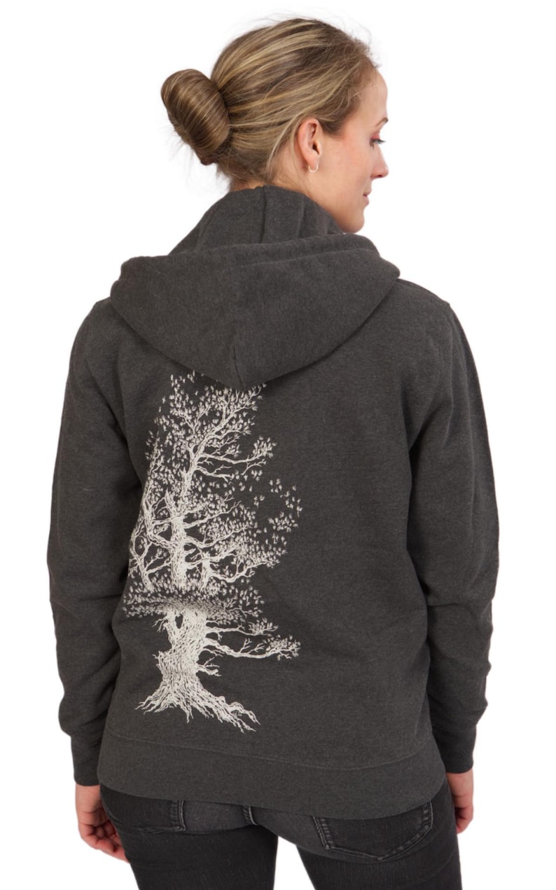 A woman wearing a gray hooded sweatshirt with a white tree design on the back.