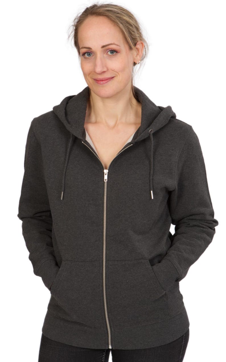 A woman wearing a gray hooded sweatshirt with her hands in her pockets, smiling at the camera.