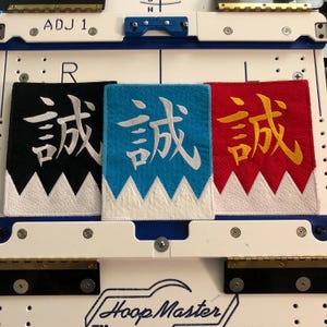 May include: Three embroidered patches with a white jagged edge and a white Chinese character on a black, blue, and red background. The character is "remarkable" in English.