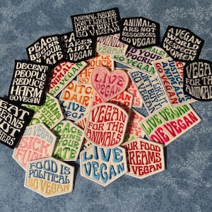 May include: A collection of embroidered fabric patches featuring various vegan-themed slogans and phrases in multiple colors, shapes, and fonts. The patches include text such as Live Vegan, Food Is Political, and Vegan For The Animals.