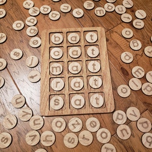 May include: Wooden game board with a grid of 12 squares, each containing a letter. The letters are 'b', 'a', 't', 'c', 'a', 't', 'm', 'a', 't', 'r', 'a', 't', 's', 'a', 't'.  There are many wooden letter tiles scattered around the board.
