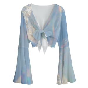 Könnte beinhalten: Ein hellblaues Crop-Top mit Schleife vorne und langen Glockenärmeln. Das Oberteil hat einen holografischen, schillernden Druck.