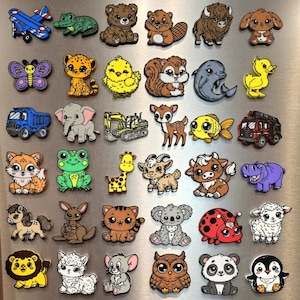 May include: A collection of colorful animal-themed magnets, including a blue airplane, a frog, a bear, a beaver, a butterfly, a cheetah, a chick, a squirrel, a dolphin, and a duck. Other magnets include a truck, an elephant, a giraffe, a deer, a fish, and a fire truck.