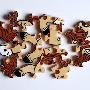 Op de afbeelding: Een voltooide puzzel met 15 stukjes, die een cartoonfiguur met bruin haar, een wit gezicht en bruine benen voorstelt. De puzzelstukjes zijn gemaakt van dik karton en hebben een glanzende afwerking.