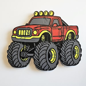 May include: A jigsaw puzzle shaped like a red monster truck with oversized gray tires, yellow wheel rims, and four yellow lights on the roof. The truck features a black grille, yellow headlights, and a dark gray windshield, assembled from multiple interlocking pieces.