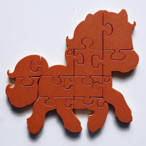 May include: A brown plastic puzzle of a horse with a mane and tail. The puzzle is made up of 10 pieces.