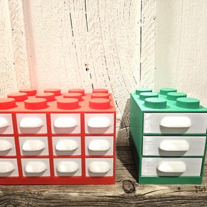 May include: Two sets of small drawers designed to resemble Lego bricks. One set is red with white drawers and the other is green with white drawers.