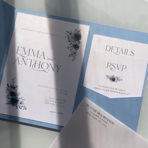 May include: A light blue wedding invitation suite with floral accents. The invitation includes the names "EMMA and ANTHONY", event details, and an RSVP card. An envelope is also included with the names "MR & MRS JASON ROGERS".