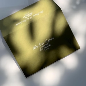 May include: An olive green envelope with white text. The envelope is addressed to "Mrs Erin Rogers" with a New York address. The top of the envelope reads "The Future Mr & Mrs Sample". The envelope is slightly open.