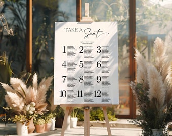 May include: A white wedding seating chart with the text "Take a Seat" and "Wedding Table" in black. The chart lists table numbers 1 through 12 with guest names under each number.