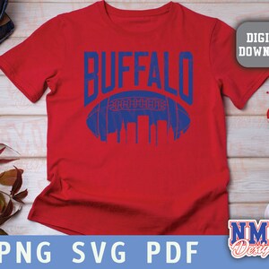Op de afbeelding: Rood T-shirt met een blauwe afbeelding van een voetbal en het woord "BUFFALO" in blauw.