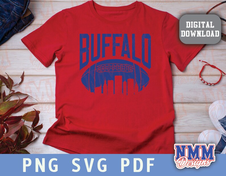 Op de afbeelding: Rood T-shirt met een blauwe afbeelding van een voetbal en het woord "BUFFALO" in blauw.