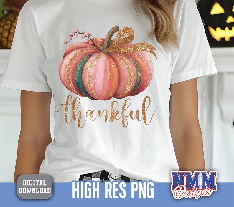May include: White t-shirt with a watercolour pumpkin design in pink, orange, and green, with gold glitter. The word "thankful" is written in gold script below the pumpkin. A digital download graphic.
