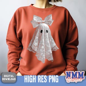 Op de afbeelding: Roestkleurig sweatshirt met een spookontwerp. Het spook is gedrapeerd in wit kant met zwarte ooguitsparingen en een grote strik. De woorden "HIGH RES PNG" zijn zichtbaar.