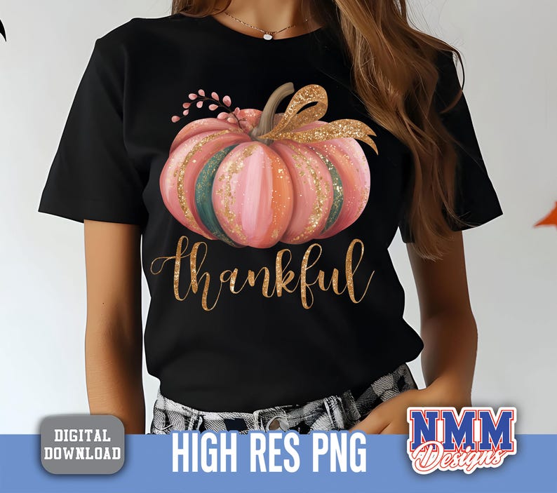 May include: Black t-shirt with a watercolour pumpkin design in pink, orange, and green, with gold glitter accents. The word "thankful" is written in gold script below the pumpkin. A fall-themed graphic tee.