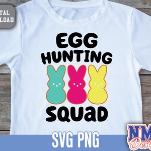 Puede incluir: Camiseta blanca con texto negro que dice "Egg Hunting Squad". Tres coloridos peeps de malvavisco en forma de conejo están debajo del texto. La camiseta se vende como descarga digital.