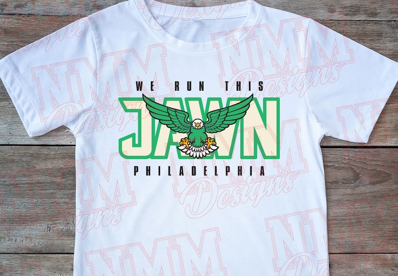 Pu&ograve; includere: Maglietta bianca con una grafica verde e crema di un'aquila con il testo "WE RUN THIS JAWN PHILADELPHIA".