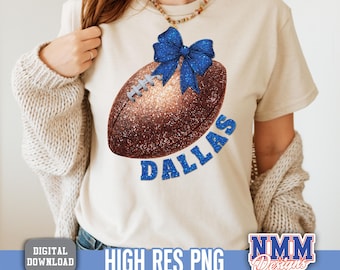 Può includere: Una maglietta beige presenta un design a forma di pallone da football con un fiocco blu e la scritta "DALLAS" in glitter blu. Il pallone è marrone con glitter e cuciture bianche. La maglietta ha una grafica scaricabile digitalmente.