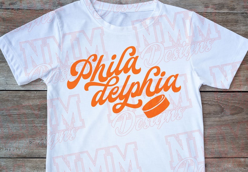 May include: White t-shirt with an orange graphic that says "Phila delphia" with a hockey puck underneath.