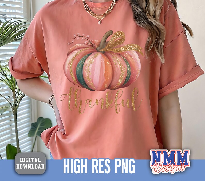 May include: A coral t-shirt with a pumpkin design in watercolour, featuring pink, orange, and green sections, with gold glitter and a gold bow. The word "Thankful" is written in gold script below the pumpkin. The shirt has rolled-up sleeves.