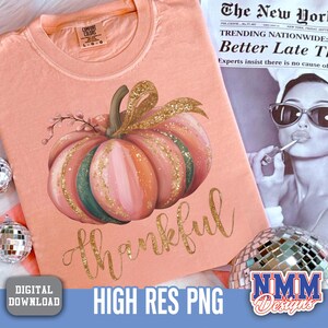 May include: A peach-coloured t-shirt with a watercolour pumpkin design in pink, green, and gold. The word "thankful" is written in gold script below the pumpkin. The shirt is a digital download, high-resolution PNG.