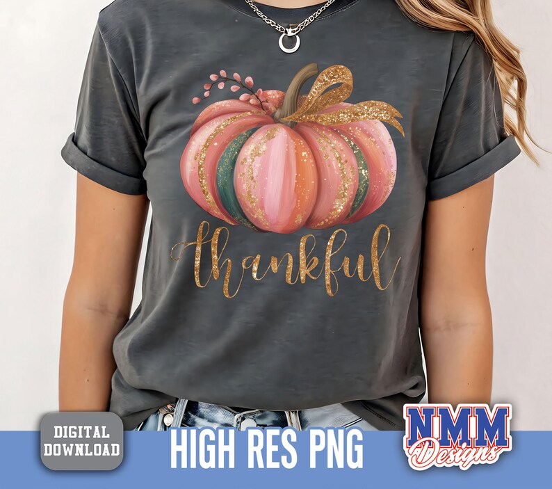 May include: Dark grey t-shirt with a watercolour pumpkin design in pink, green, and gold. The word "thankful" is written in gold script below the pumpkin. A digital download graphic.