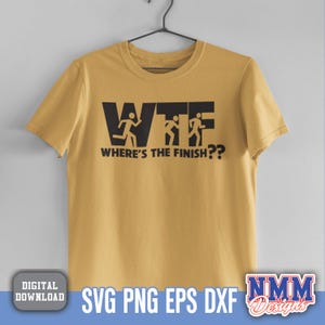 Puede incluir: Camiseta de color amarillo mostaza con el texto negro "WTF WHERE'S THE FINISH??". El dise&ntilde;o presenta figuras de palo corriendo dentro de las letras. La camiseta est&aacute; colgada de una percha negra.