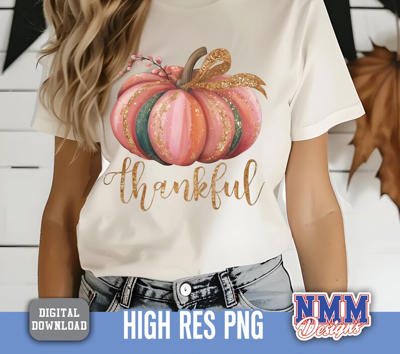 May include: Cream-coloured t-shirt with a watercolour pumpkin design in pink, orange, and green, with a gold glitter bow and the word "thankful" in gold script. Digital download.