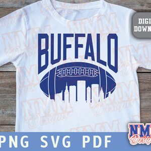 Op de afbeelding: Een wit T-shirt met een blauw en wit ontwerp van een voetbal met het woord "BUFFALO" erboven. De voetbal bevat een skyline erin.