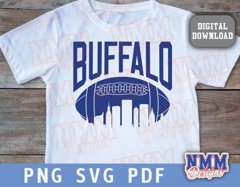 Op de afbeelding: Een wit T-shirt met een blauw en wit ontwerp van een voetbal met het woord "BUFFALO" erboven. De voetbal bevat een skyline erin.