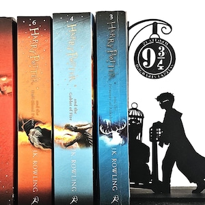 Könnte beinhalten: Vier Harry Potter Bücher mit farbenfrohen Einbänden, darunter "Harry Potter und der Feuerkelch" und "Harry Potter und der Gefangene von Askaban". Ein schwarzer Metall-Buchstütze zeigt Bahnsteig 9 3/4 und eine Silhouette.