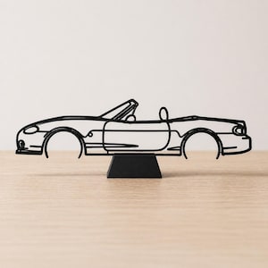 Può includere: Una scultura in filo di metallo nero di un'auto cabriolet. Il design minimalista mostra il contorno dell'auto, comprese le ruote, le portiere e la capote. La scultura è montata su una piccola base nera, creando un'esposizione artistica moderna.