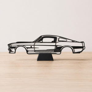 May include: A black and white car silhouette, a classic sports car design, is displayed on a black stand. The car's body is white, with black outlines defining the details. The wheels are not present, giving it a unique, artistic look.