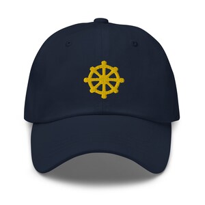 Puede incluir: Una gorra de b&eacute;isbol azul marino con un s&iacute;mbolo Dharmachakra bordado en oro.