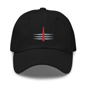 May include: A black baseball cap with an embroidered red and gray symbol on the front. The symbol is a stylized representation of the Hindu god Shiva's trident.