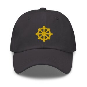 Puede incluir: Una gorra de b&eacute;isbol negra con un s&iacute;mbolo Dharmachakra bordado en oro.