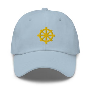 Puede incluir: Una gorra de b&eacute;isbol azul claro con un s&iacute;mbolo Dharmachakra bordado en amarillo.