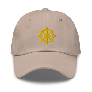 Puede incluir: Una gorra de b&eacute;isbol beige con un s&iacute;mbolo Dharmachakra bordado en amarillo.