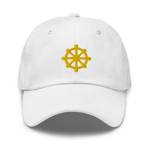 Puede incluir: Una gorra de b&eacute;isbol blanca con un s&iacute;mbolo Dharmachakra bordado en oro.