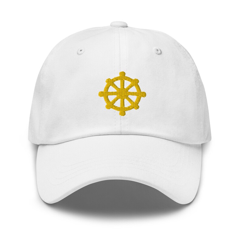 Puede incluir: Una gorra de b&eacute;isbol blanca con un s&iacute;mbolo Dharmachakra bordado en oro.