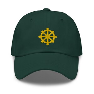 Puede incluir: Una gorra de b&eacute;isbol verde oscuro con un s&iacute;mbolo Dharmachakra bordado en oro.
