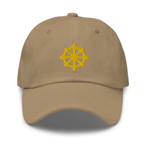 Puede incluir: Una gorra de b&eacute;isbol de color beige con un s&iacute;mbolo Dharmachakra bordado en amarillo en la parte delantera.