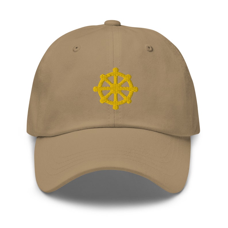 Puede incluir: Una gorra de b&eacute;isbol de color beige con un s&iacute;mbolo Dharmachakra bordado en amarillo en la parte delantera.