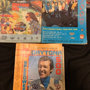 Puede incluir: Tres portadas de programas de carreras vintage de Daytona 500. La primera portada es azul y presenta un grupo de personas en las gradas. La segunda portada es amarilla y presenta un coche de carreras. La tercera portada es naranja y presenta a un piloto con un traje de carreras.