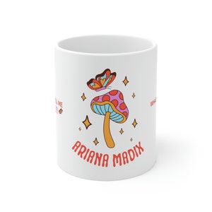 Könnte beinhalten: Weiße Keramiktasse mit einem bunten Pilz- und Schmetterlingsmotiv. Der Text "Ariana Madix" ist unter dem Pilz aufgedruckt.
