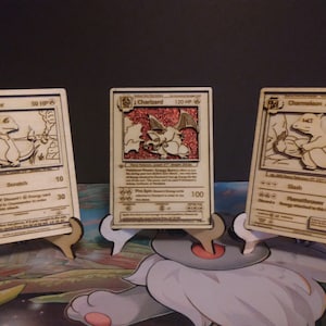May include: Three wooden Pokemon trading cards featuring Charmander, Charmeleon, and Charizard. The cards are laser cut and have a wood grain finish. The Pokemon are depicted in their classic artwork.
