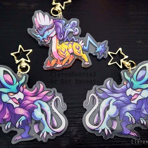 Puede incluir: Tres llaveros de personajes de estilo de dibujos animados, inspirados en el anime, coloridos. Los llaveros están hechos de acrílico transparente con un diseño impreso. Los personajes son una criatura azul y amarilla con una melena blanca, una criatura morada y azul con una melena turquesa y una criatura morada y azul con una melena turquesa. Los llaveros tienen dijes dorados en forma de estrella.